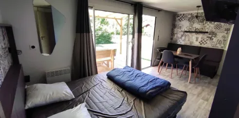 Chambre du mobil home avec lit, rideaux et accès à la terrasse - Family's Camping Le Savoy