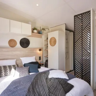 Mobil Home Tahiti Premium 3 Chambres 6 Personnes SPA - Landrezac Plage : chambre avec lit, étagères et décoration
