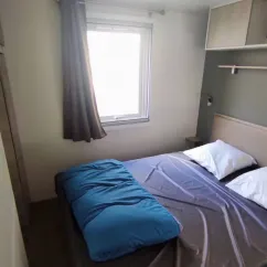 Chambre du Mobil Home Confort 3 Chambres Family's Camping Le Savoy avec lit, couvre-lits bleu et fenêtre