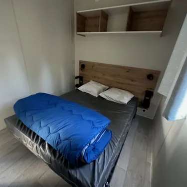 Mobil Home Confort 3 Chambres 6 Personnes - Family's Camping Le Savoy : lit avec couette bleue et étagères murales