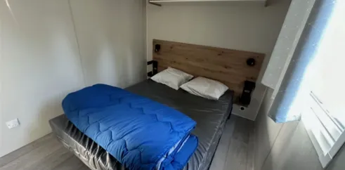 Mobil Home Confort 3 Chambres 6 Personnes - Family's Camping Le Savoy : lit avec couette bleue et étagères murales