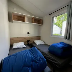 Mobil Home Confort 3 Chambres 6 Personnes - Family's Camping Le Savoy : deux lits avec couettes bleues et fenêtre