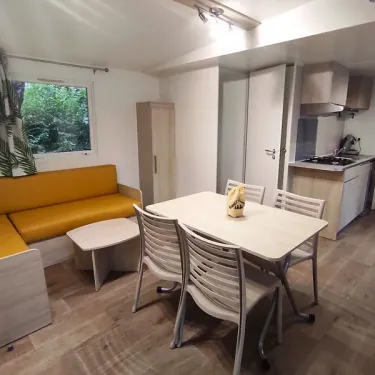 Salon avec canapé jaune, table et cuisine - Mobil Home Confort - Family's Camping Le Savoy