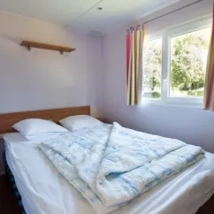 Chambre dans le Mobil Home Confort Tuffault, lit double, rideaux colorés, étagère murale.