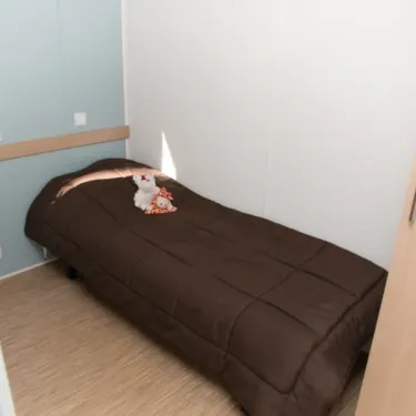 Chambre simple dans le mobil home Eden Thouet, avec couverture marron et ours en peluche.