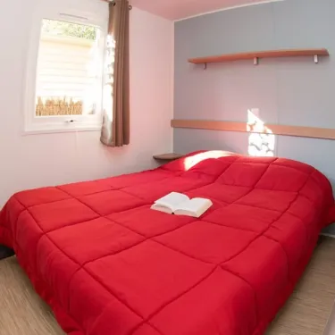 Chambre avec lit double rouge, livre ouvert, et étagères murales dans le mobil home Eden Maine.