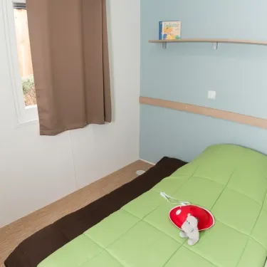 Chambre mobil home Eden Loire 3 chambres, lit vert, rideau marron, étagère murale