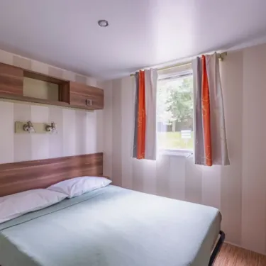 Chambre avec lit double et rideaux orange dans le camping Paradis Domaine de Gaujac