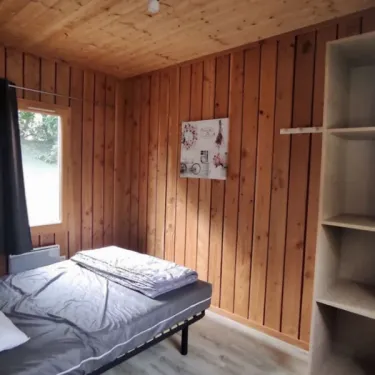 Chambre du chalet PMR avec lit simple, mur en bois et étagères.