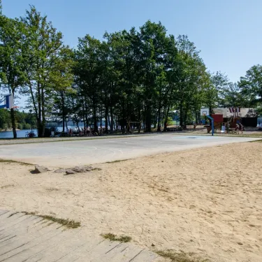 Plage de sable avec arbres et eau au loin au Camping Paradis Les 2 Îles