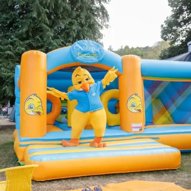 Personnage de poule jaune sur un manège gonflable orange et bleu au Camping Paradis Les 2 Îles