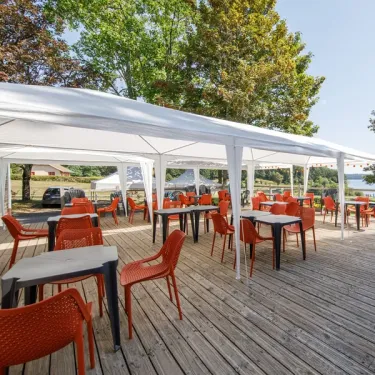 Terrasse extérieure sous une tente blanche avec tables et chaises rouges sur bois.