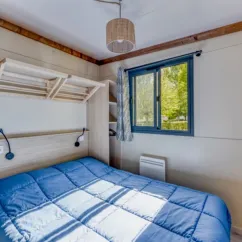 Chambre du Cottage Premium avec lit, étagères et vue lac - Camping Paradis Les 2 Îles