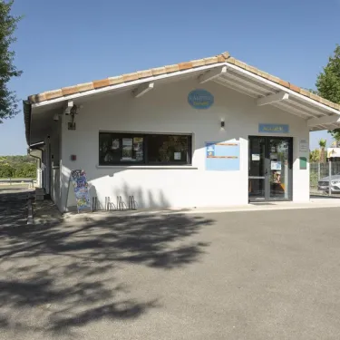 Bureau du Camping Paradis Albret sous un ciel bleu, avec des arbres en arrière-plan.