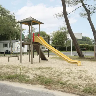 Piste de jeux pour enfants au Camping Paradis Albret, avec toboggan jaune et cabane en bois.