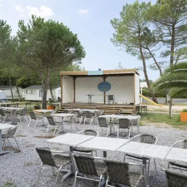 Terrasse extérieure du Camping Paradis Albret avec tables, chaises et scène en bois.