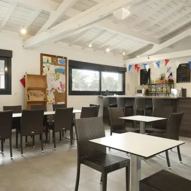 Salle de repas du Camping Paradis Albret avec tables et chaises en plastique noir.