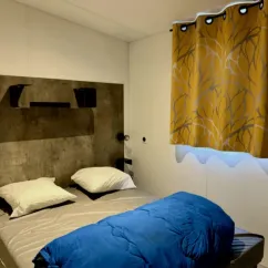 Mobil Home Premium 4 Chambres 8 Personnes - Paradis Family des Issoux : chambre avec lit et rideaux jaunes