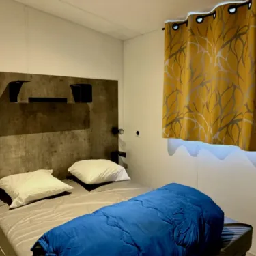 Mobil Home Premium 4 Chambres 8 Personnes - Paradis Family des Issoux : chambre avec lit et rideaux jaunes