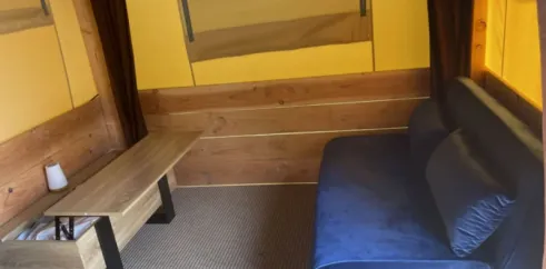Tente Baroudeur 1 Chambre 2 Personnes Sans Sanitaires - Paradis Family des Issoux : canapé bleu, banc en bois et mur en bois