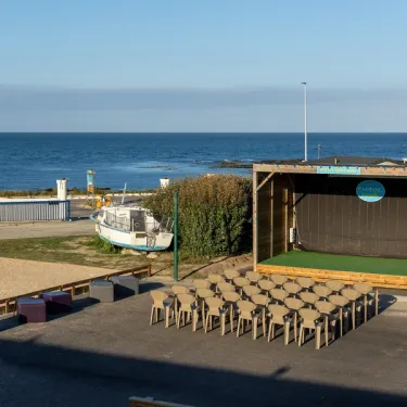 Camping Paradis La Baie de Ploemeur : scène en plein air avec chaises et bateau au bord de la mer.