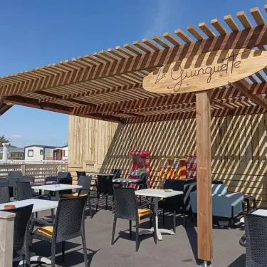 Camping Paradis La Baie de Ploemeur : terrasse ombrée avec tables et chaises sous une pergola en bois.