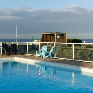 Piscine entourée d'une clôture blanche avec chaise bleue près du bord de mer.