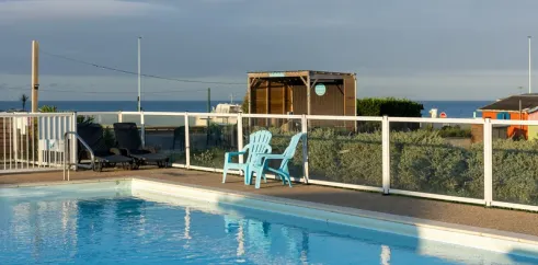 Piscine entourée d'une clôture blanche avec chaise bleue près du bord de mer.