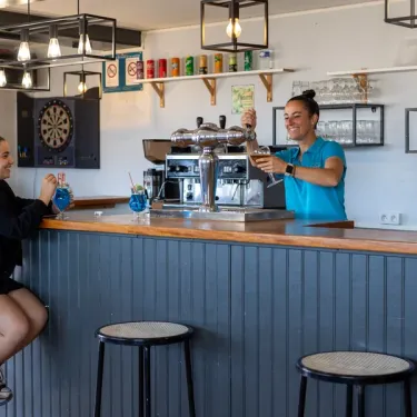 Camping Paradis La Baie de Ploemeur : bar avec serveuse et verres à cocktails sur un comptoir en bois.