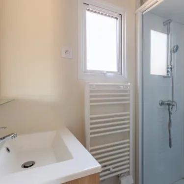 Salle de bain avec lavabo, radiateur et douche dans le mobile home MH Premium 3CH – 6P (Sam) - Camping Paradis la Baie de Ploemeur