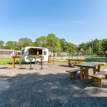 Camping Bel Air Village le Brabois : camionnette et tables en bois sur pelouse