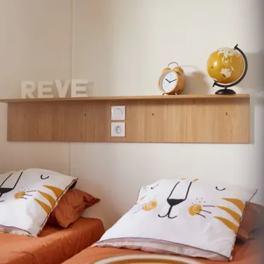 Lit double avec oreiller de lion et étagère dans MH Confort+ 3CH – 6P - Camping Bel Air Village Le Brabois