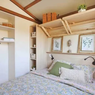 Chambre cottage avec lit double et étagères dans Cottage Premium 3CH – 6P - Camping Bel Air Village Le Brabois