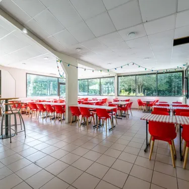 Salle à manger du Camping Paradis Le Coiroux avec tables et chaises rouges.