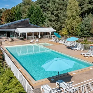 Piscine extérieure du Camping Paradis Le Coiroux entourée de transats et d'ombrelles bleues.