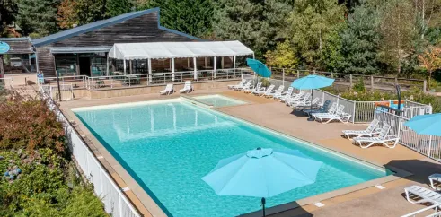 Piscine extérieure du Camping Paradis Le Coiroux entourée de transats et d'ombrelles bleues.