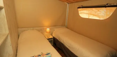 Lodge Maasaï 2CH – 4P - Camping Paradis Le Coiroux : deux lits, lampe de chevet