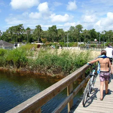 Camping Les Viviers : personne avec vélo sur pont en bois au-dessus d'eau