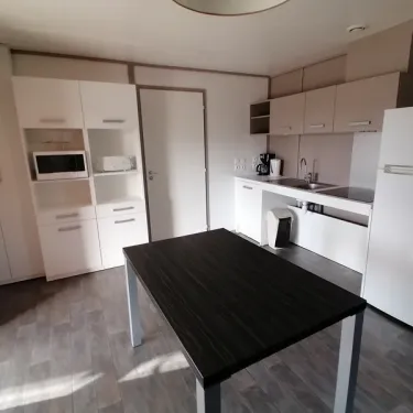 Cottage Premium PMR 2CH – 4P - Camping Bel Air Village Les Demeures du Lac, cuisine moderne avec table et réfrigérateur