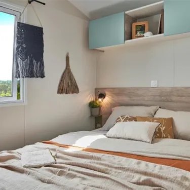 Lit double avec couvre-lit beige et décorations suspendues dans Mobil Home Bahia Modulo Confort