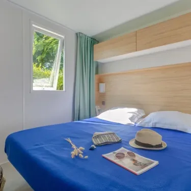Chambre avec lit double bleu, Mobil Home Bora Bora, Camping La Touesse, rideaux verts, tablette