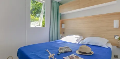 Chambre avec lit double bleu, Mobil Home Bora Bora, Camping La Touesse, rideaux verts, tablette