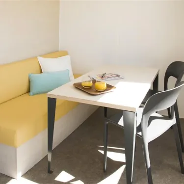 Mobil Home Cahita 1 Chambre 2 Personnes- Camping La Touesse : canapé jaune, table, chaises