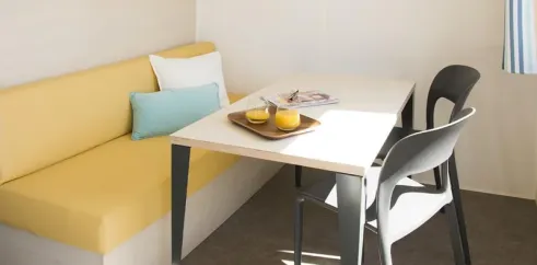 Mobil Home Cahita 1 Chambre 2 Personnes- Camping La Touesse : canapé jaune, table, chaises