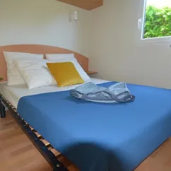 Mobil Home Flores 2 Chambres 4 Personnes- Camping La Touesse : lit double, drap bleu, fenêtre