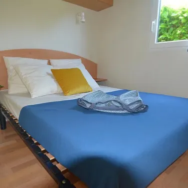 Mobil Home Flores 2 Chambres 4 Personnes- Camping La Touesse : lit double, drap bleu, fenêtre