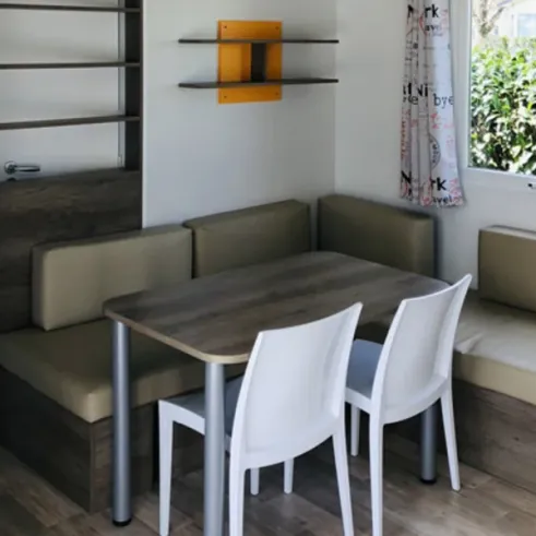 Table à manger avec chaises blanches et canapé en mobil-home - Camping Paradis de Rhuys