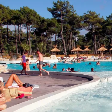 Personnes autour d'une piscine avec parasols en paille et arbres de pins
