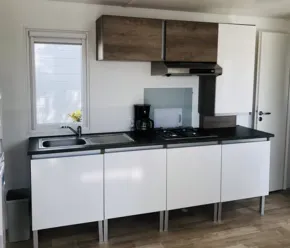 Mobil Home Premium 2 Chambres 4 Personnes 28m² - Camping Paradis de Rhuys : cuisine équipée avec plan de travail noir et armoires blanches