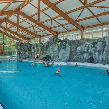 Camping Ty Nadan : piscine couverte avec une paroi rocheuse et des visiteurs nageant.